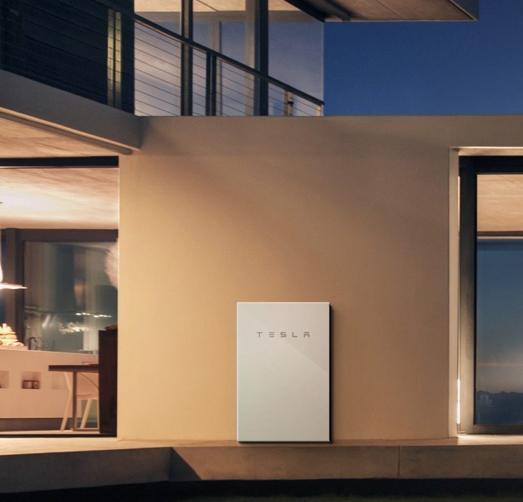 A tesla electric car is parked in front of a house at night.