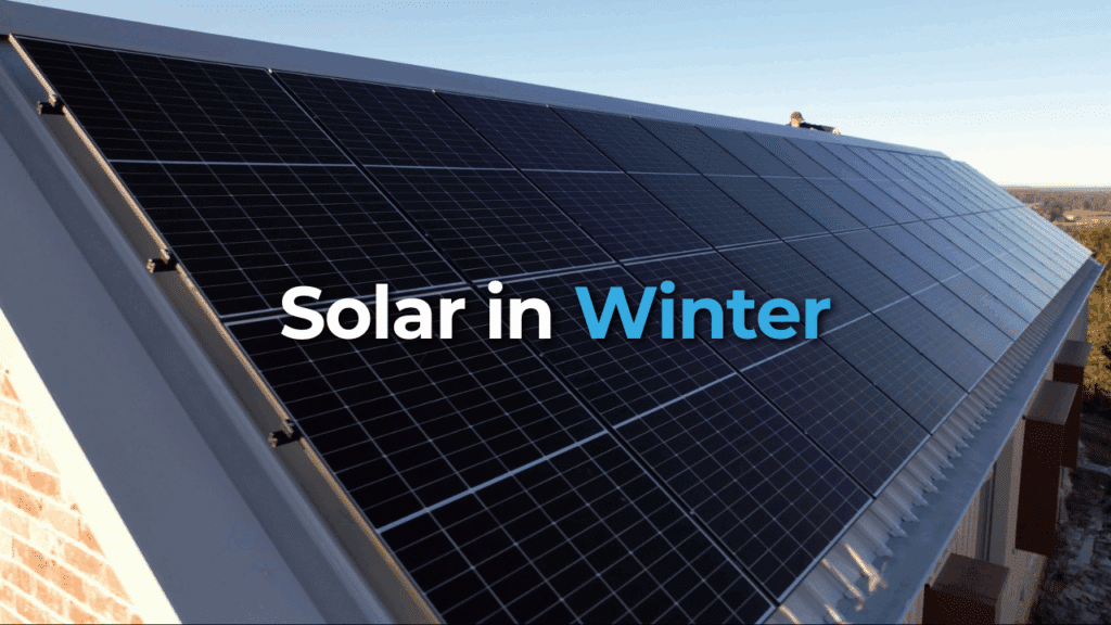 A row of dark solar panels installed on a slanted rooftop under clear sky, with the text "Solar in Winter" overlaid on the image.