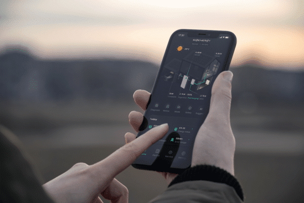 Person using a smartphone with a smart home control app displayed, showing data and settings related to energy usage.